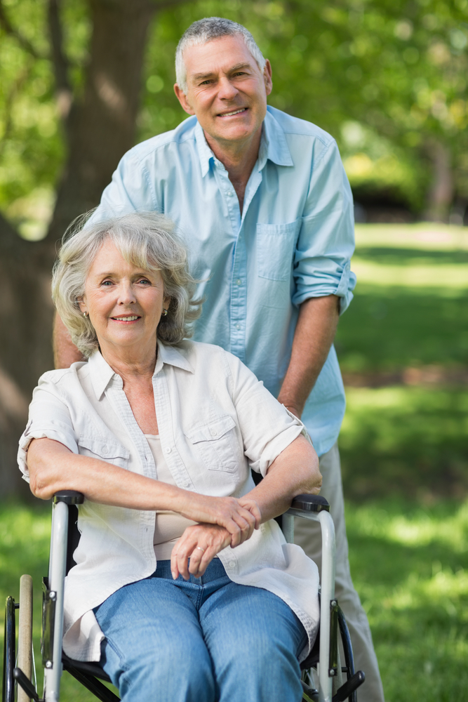Portrait of a smiling mature man with woman sitting in wheel chair at the park