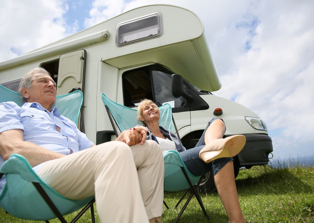 Senior couple relaxing in camping folding chairs, camper in background